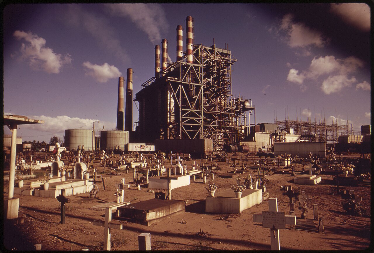 Oil-fired Palo Seco power plant with striped chimneys and steel frame rising behind a cemetery across the bay from San Juan
