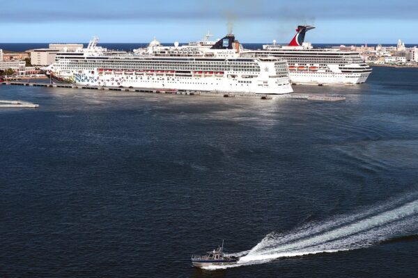 Two cruise ships docked at the San Juan cruise piers beside Old San Juan, with a small boat crossing the harbour in the foreground