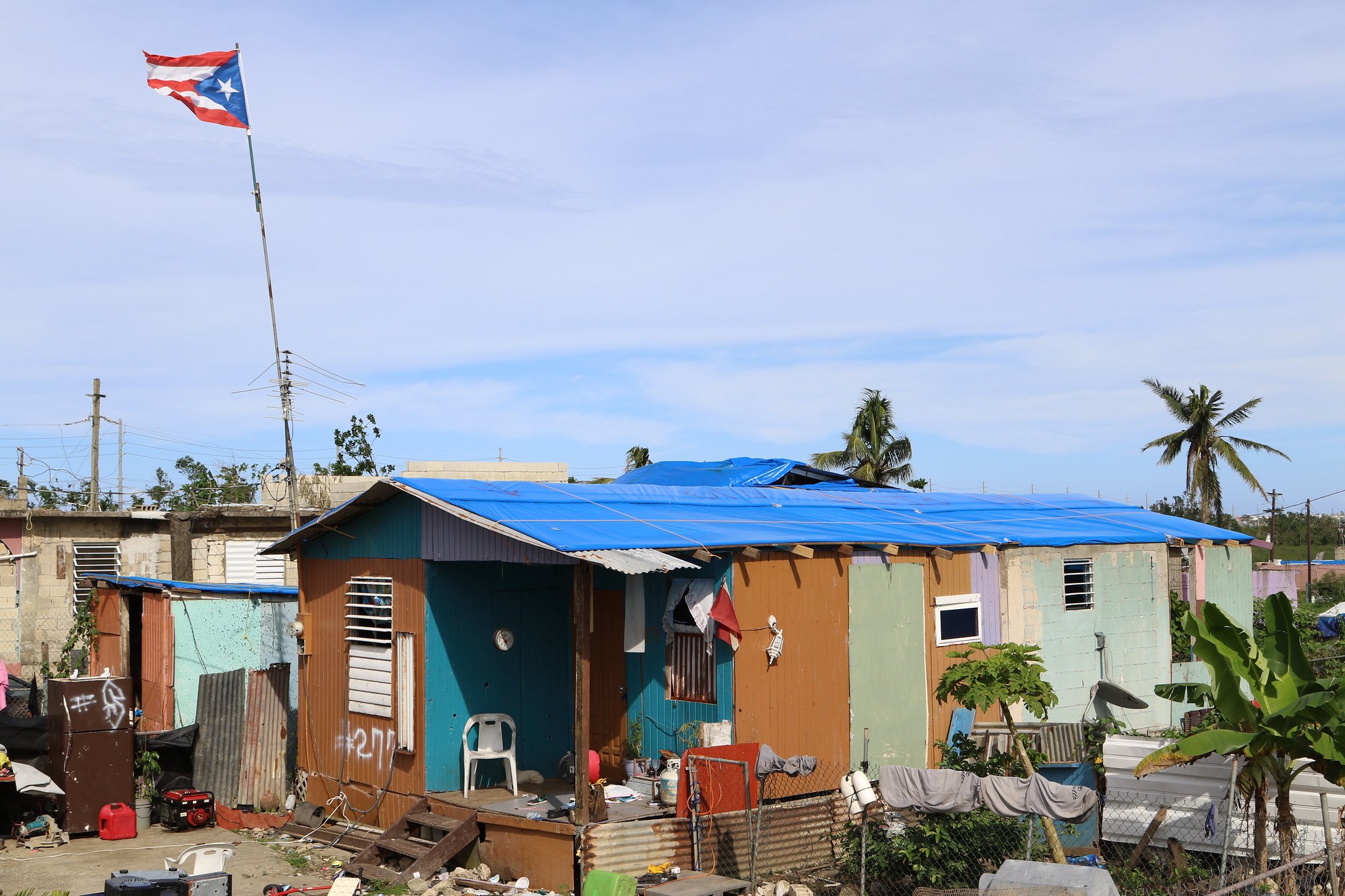 House in Puerto Rico with a blue tarp covering its roof and a Puerto Rican flag flying above it after Hurricane Maria