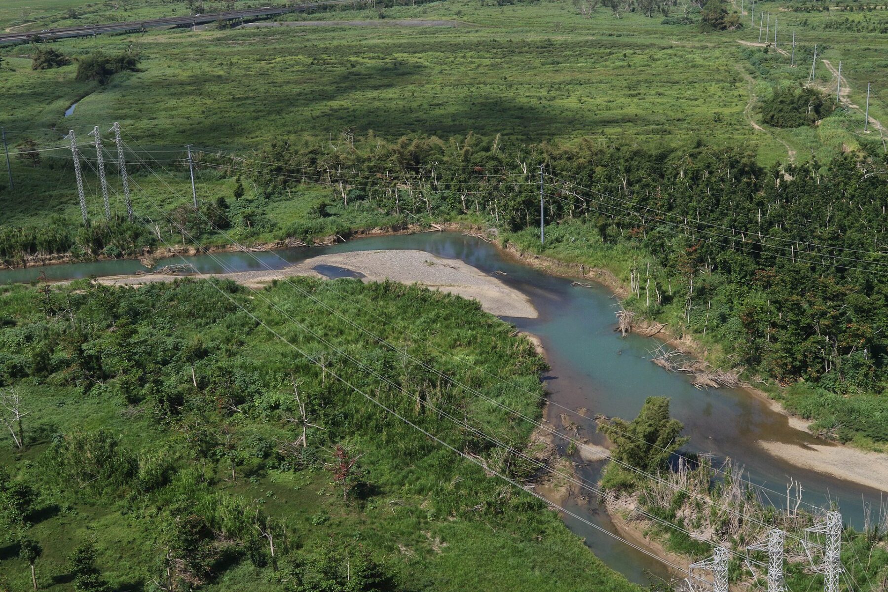 Aerial view of power lines and steel transmission towers crossing a green river valley in Puerto Rico