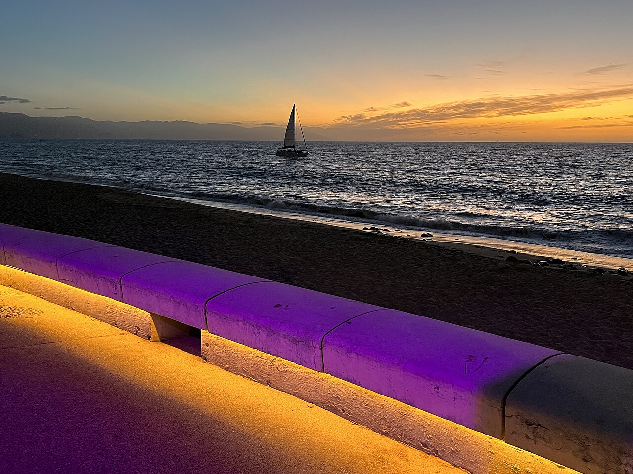 Sailboat at sunset on Banderas Bay seen from the beach and seawall of the Malecón in Puerto Vallarta