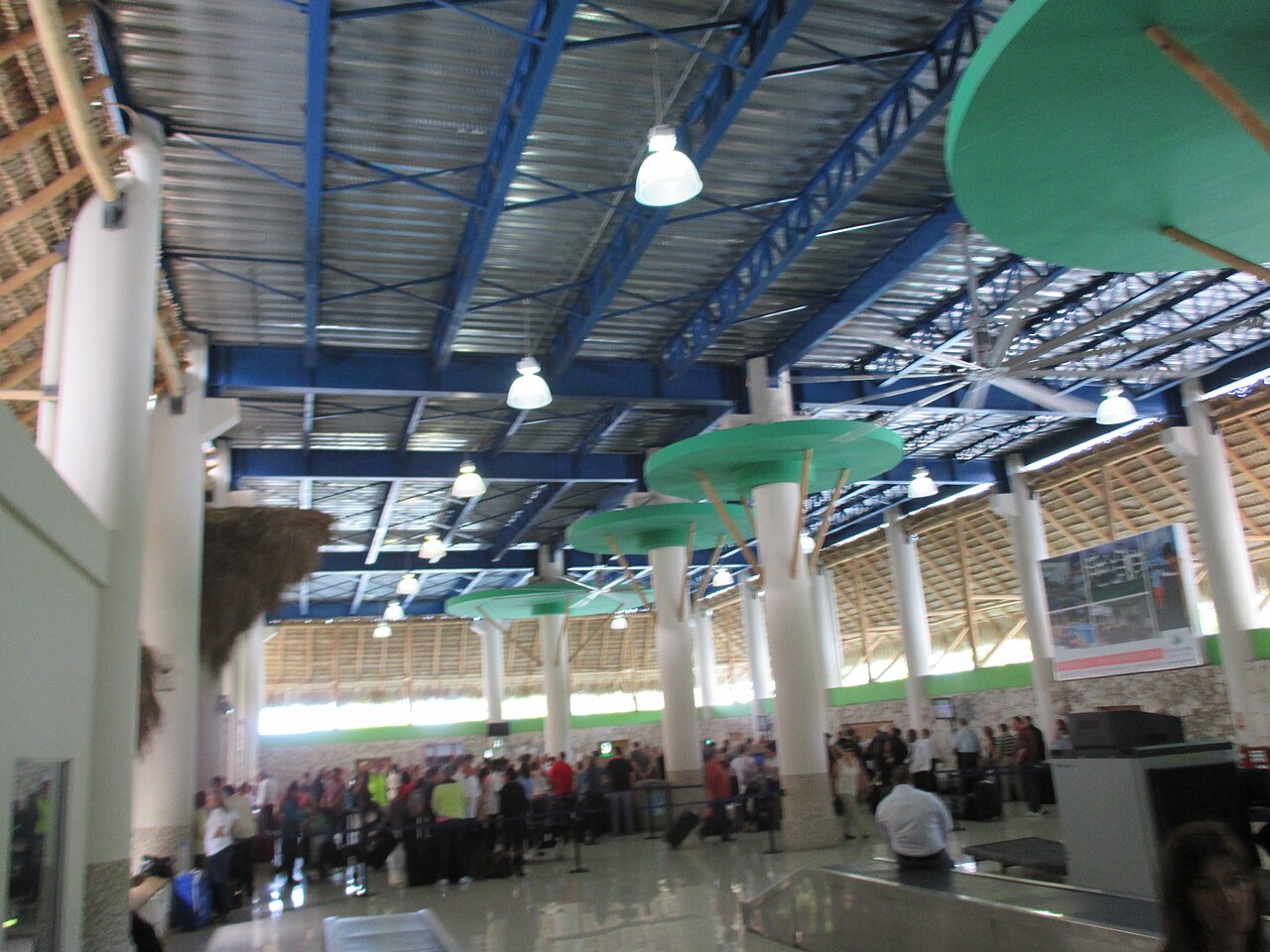 Travellers queue in the arrival hall of Punta Cana International Airport under a blue steel roof.