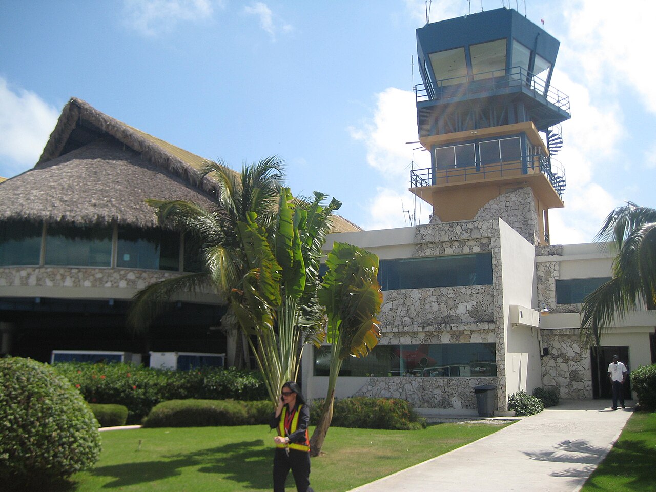 Thatched terminal building and control tower at Punta Cana International Airport, with palms and a stone-clad annex.