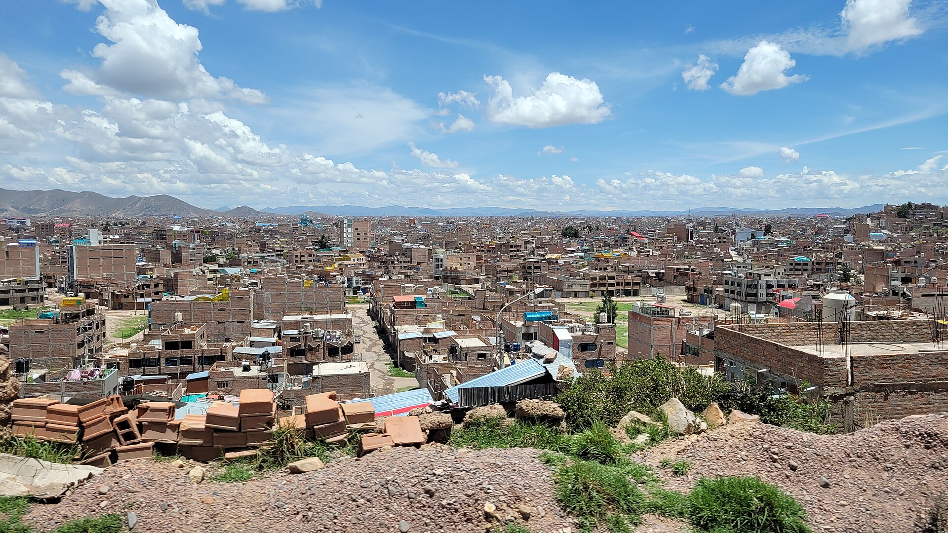 Rows of brick houses, many unfinished, spreading across the flat highland city of Juliaca under a blue sky with hills on the horizon