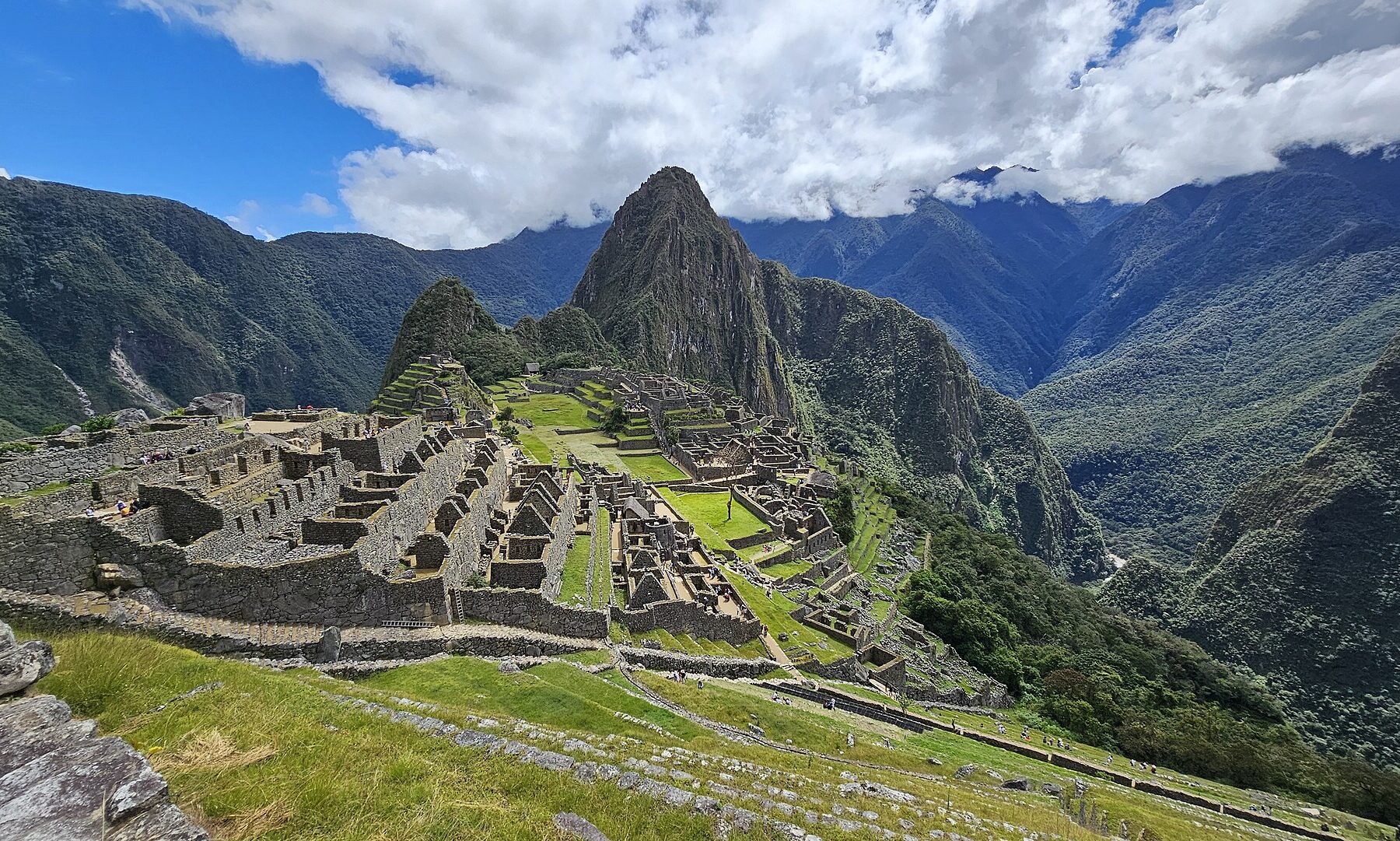 Stone terraces and ruined buildings of the Inca citadel of Machu Picchu below the peak of Huayna Picchu and forested Andean mountains