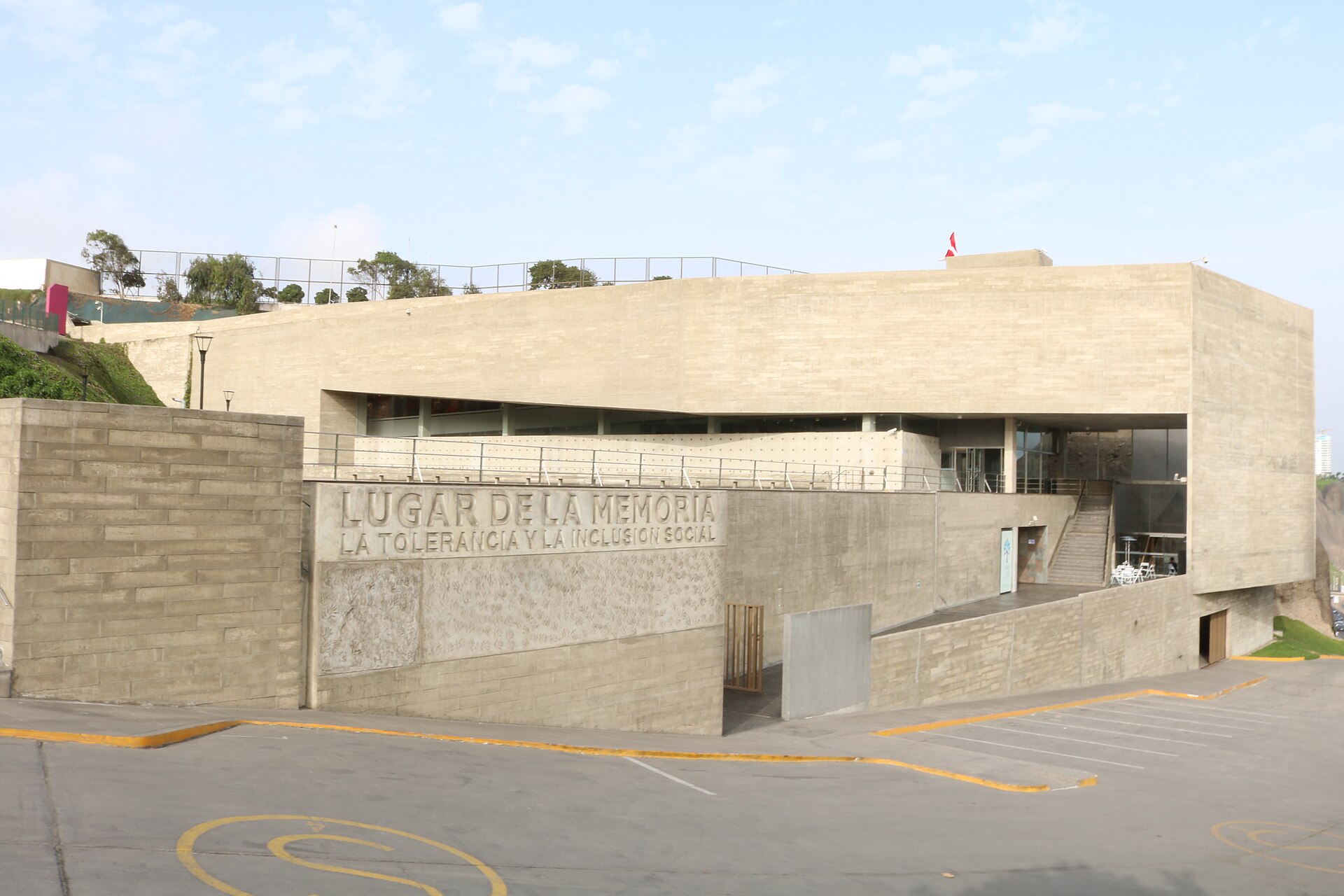 Concrete building of the Lugar de la Memoria museum in Lima with its name carved on the facade and a Peruvian flag on the roof