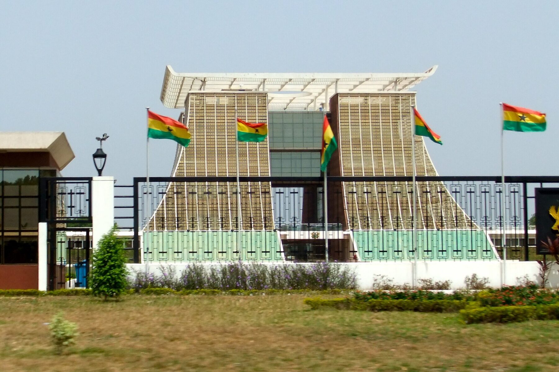 Ghana's Golden Jubilee House, the presidential palace in Accra, seen behind a fence lined with Ghanaian flags under a hazy sky
