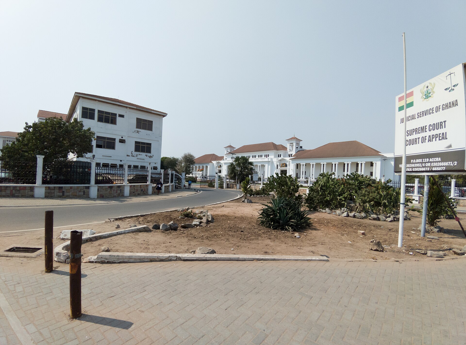 The white Supreme Court building in Accra with red-tiled roofs, behind a landscaped roundabout and a Judicial Service of Ghana sign reading Supreme Court, Court of Appeal