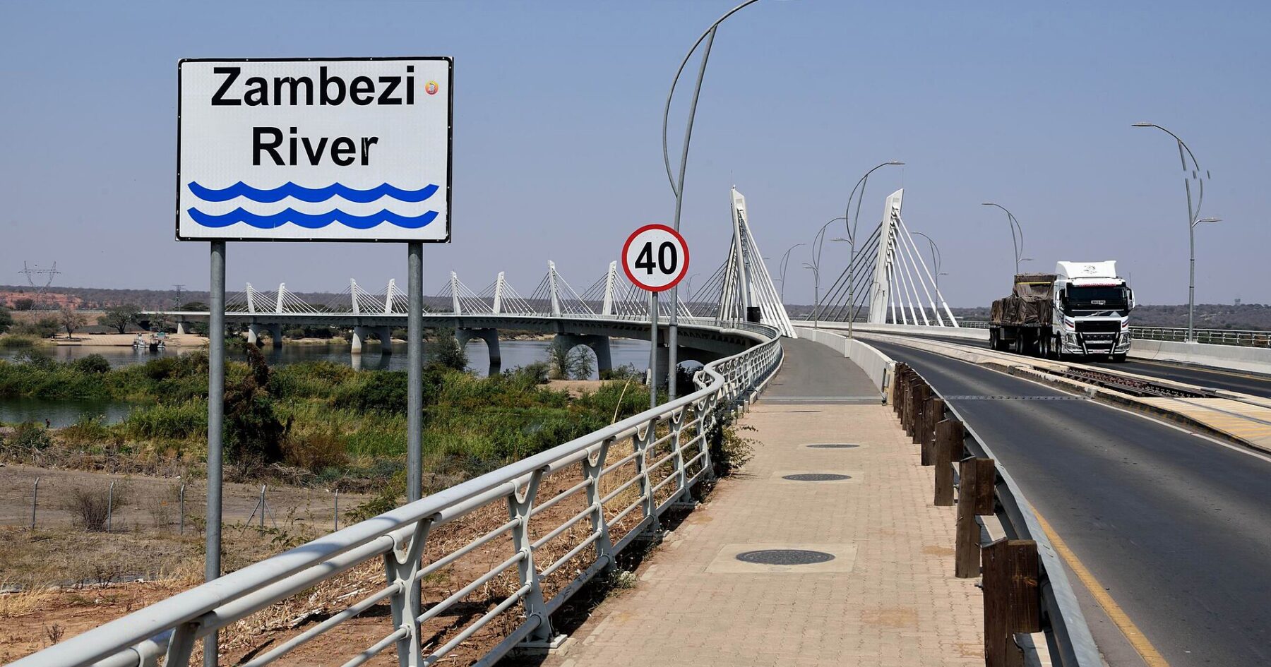 A lorry crosses the white cable-stayed Kazungula Bridge over the Zambezi River, beside a road sign reading Zambezi River and a 40 km/h limit