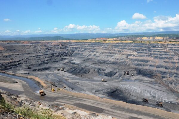 Open-pit Cerrejón coal mine in La Guajira with haul trucks on terraced grey benches under a blue sky with white clouds
