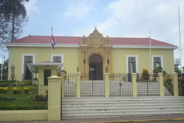 The yellow neo-colonial Casa Amarilla in San José, with a red roof, an ornate central doorway, a Costa Rican flag, and wide steps behind an iron fence