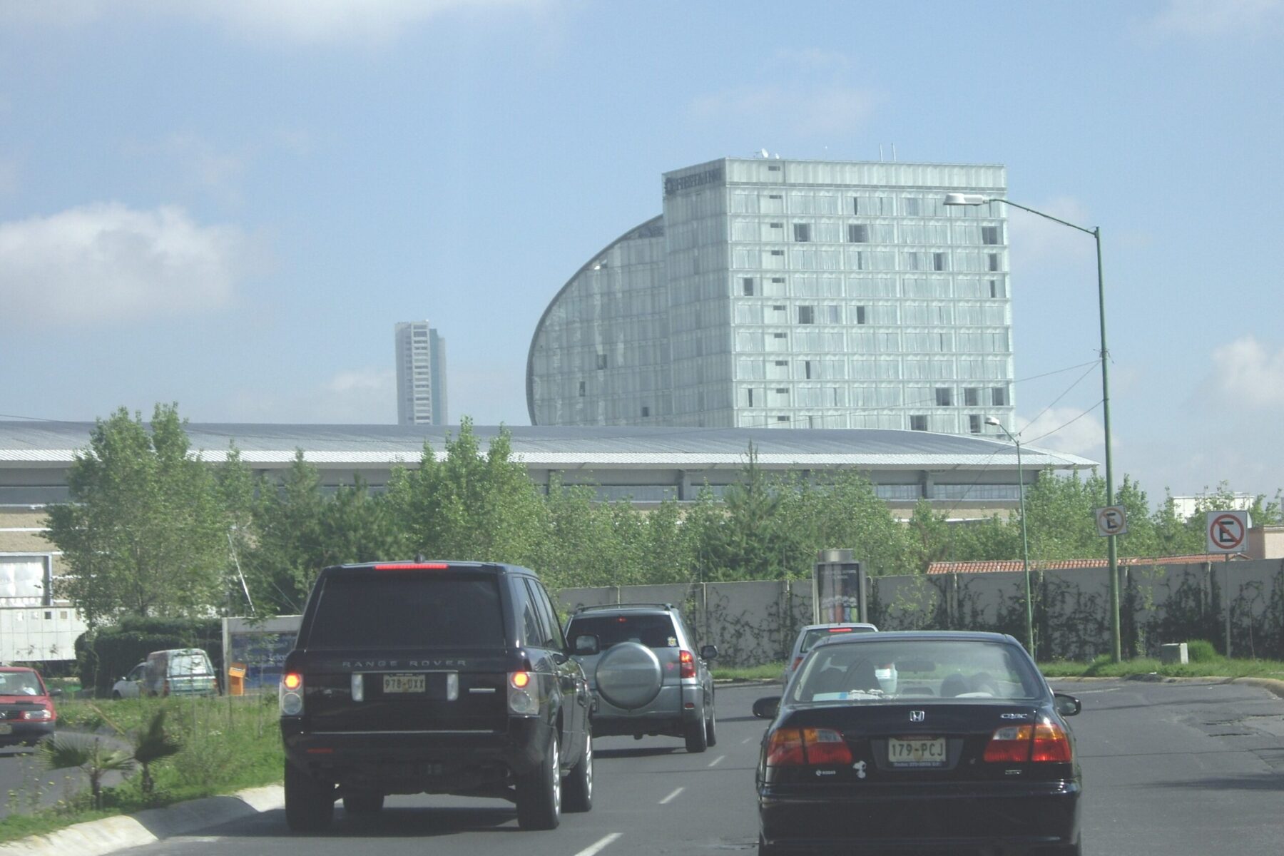 Cars drive along a Mexico City avenue in front of a glass hotel tower