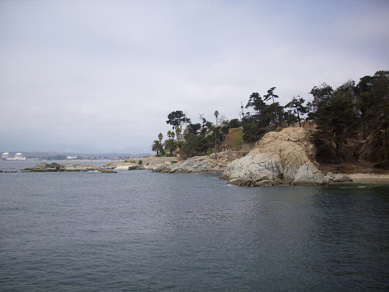 Rocky coastline of Quintero in Chile's Valparaíso region, with industrial gas tanks visible in the distance