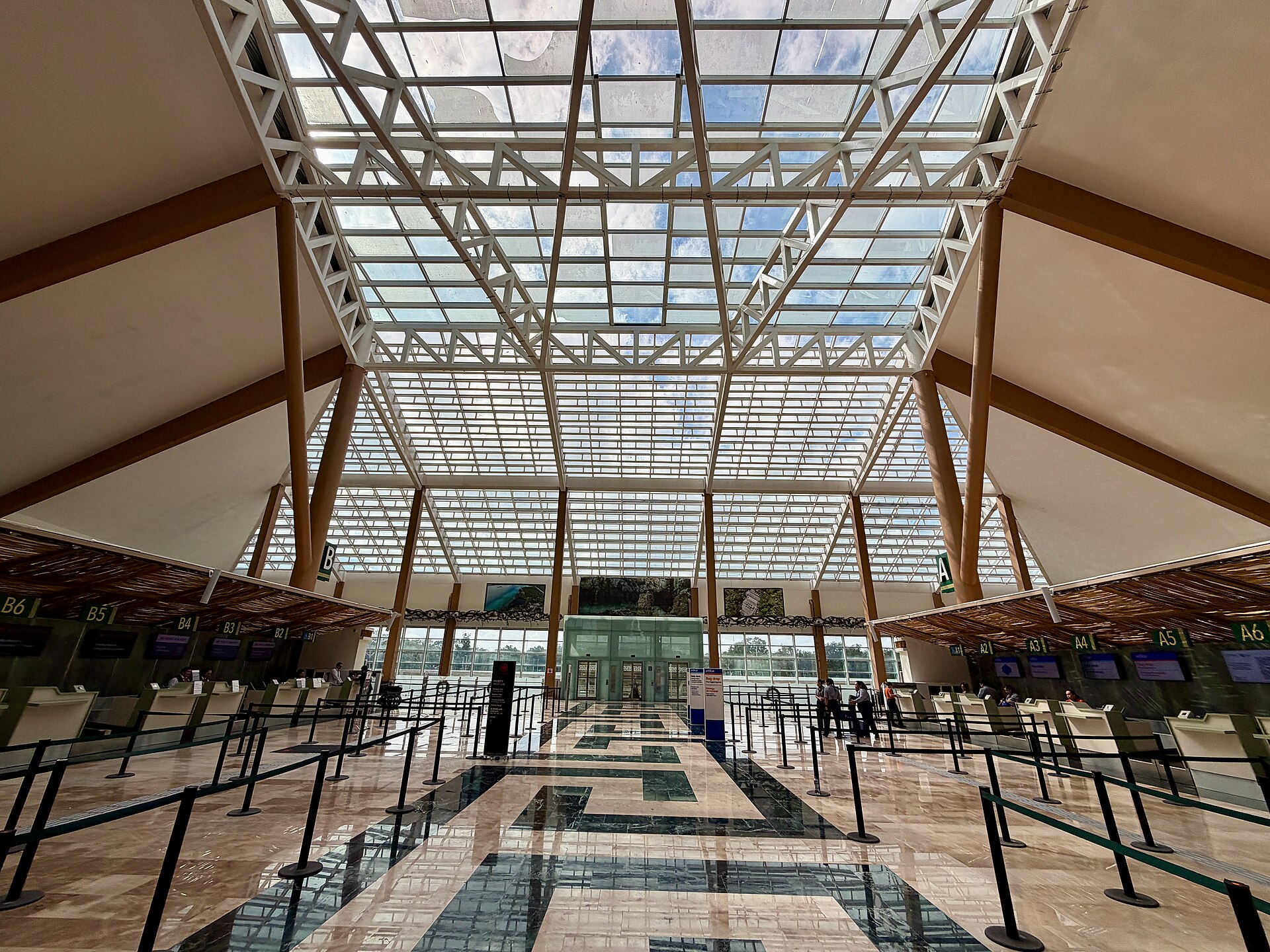 Check-in hall with a glass roof, wooden pillars and queue barriers inside Tulum airport