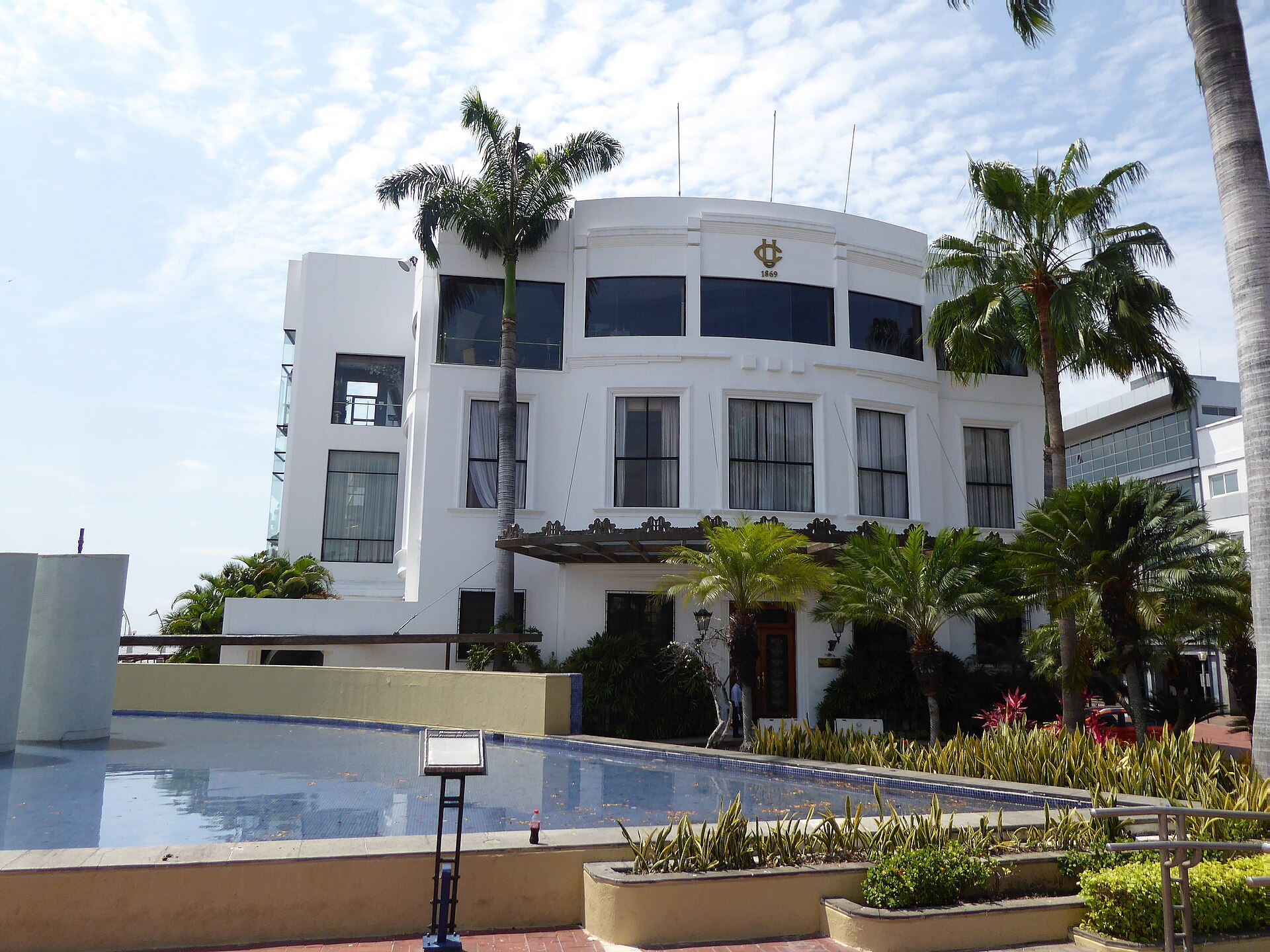 The white curved Club de la Union building on the Malecon in Guayaquil, framed by palm trees and a reflecting pool under a pale sky