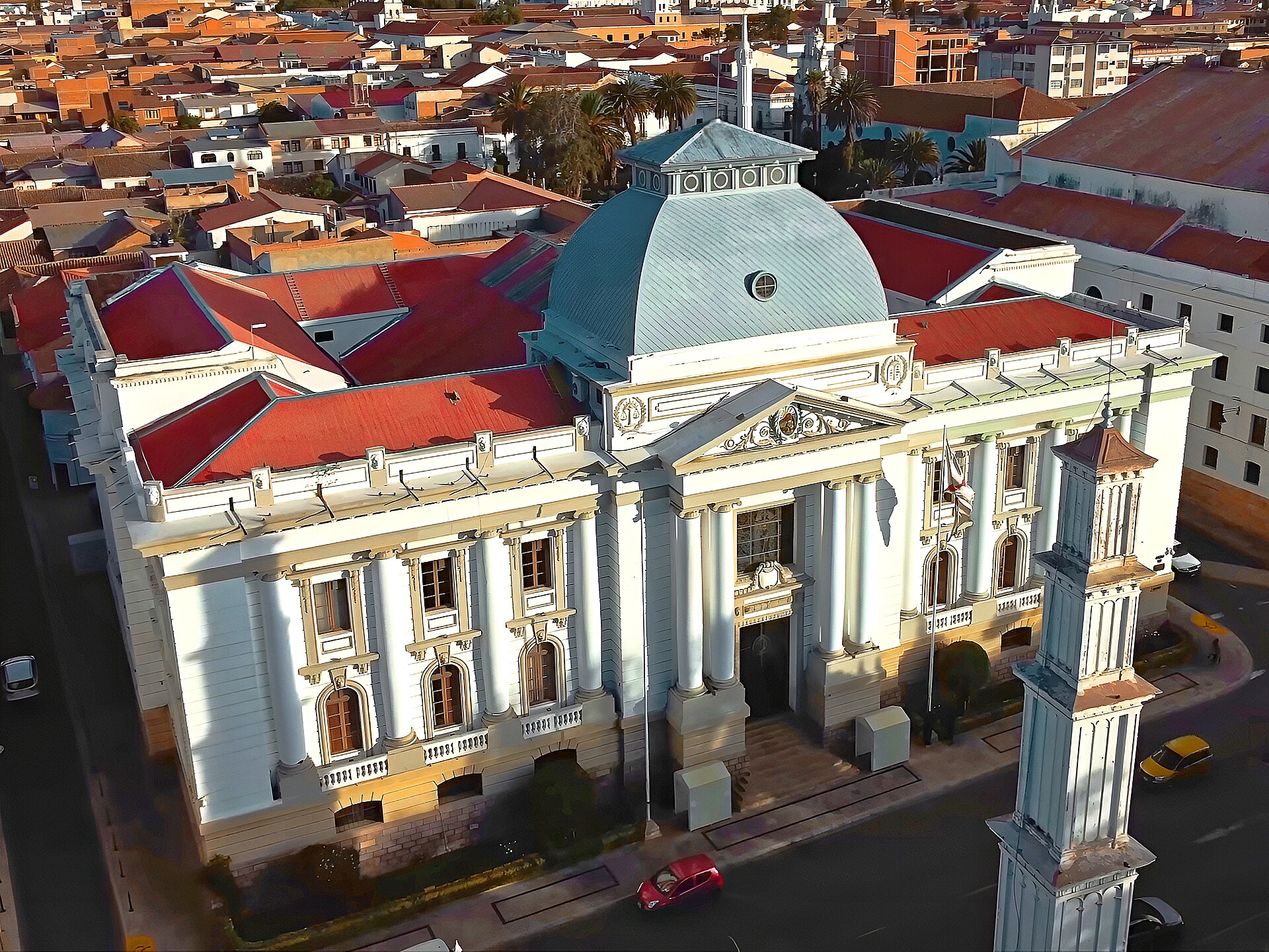 Aerial view of the domed Supreme Court building in Sucre with red tile roofs, a white tower and city streets around it
