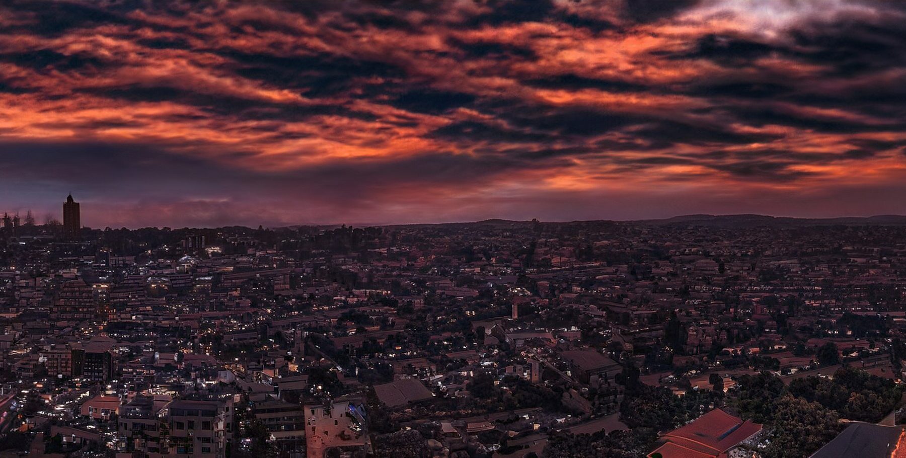 Evening view over Kampala rooftops and a tower under a dark orange and purple cloudy sky