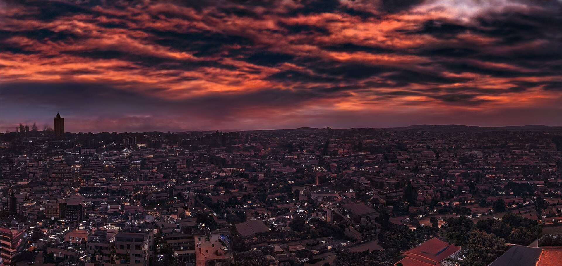Evening view over Kampala rooftops and a tower under a dark orange and purple cloudy sky