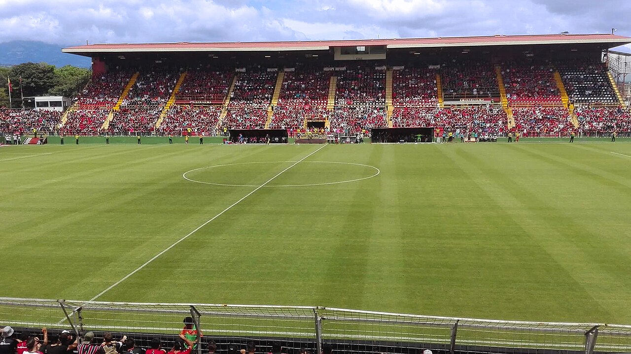 The Estadio Alejandro Morera Soto in Alajuela, Costa Rica, with a full red-and-black stand behind a green pitch