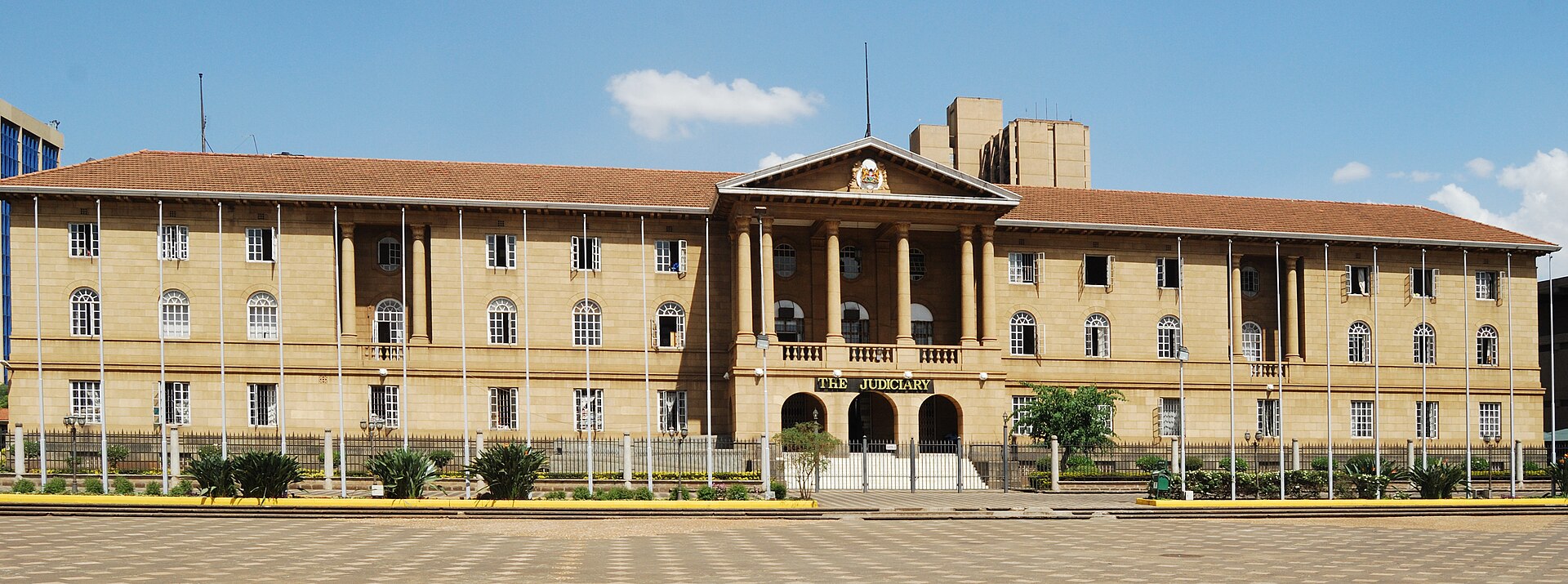 The Kenya Judiciary building in Nairobi, a two-storey stone building with a red tiled roof and columned entrance under a blue sky