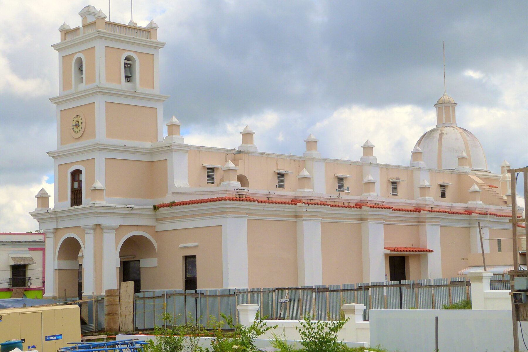 The cream and pale yellow Iglesia de Nuestra Senora de la Asuncion in Cayey, with a bell tower, a dome and a cloudy sky