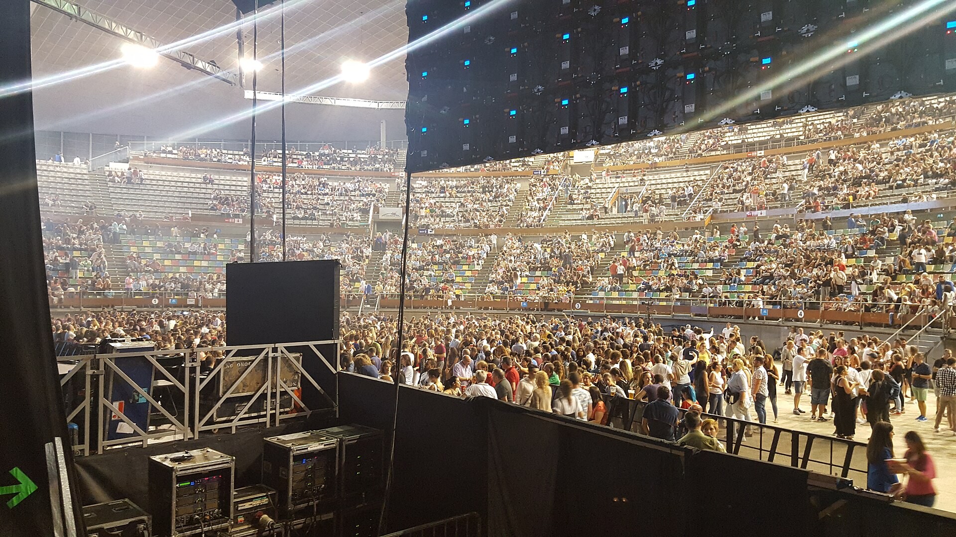 A large crowd in an indoor arena before a concert, seen from beside the stage