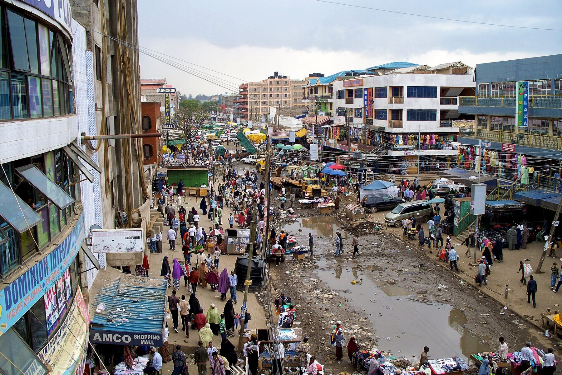 Crowded street market in Eastleigh, Nairobi, with shops, stalls and multi-storey buildings under a cloudy sky