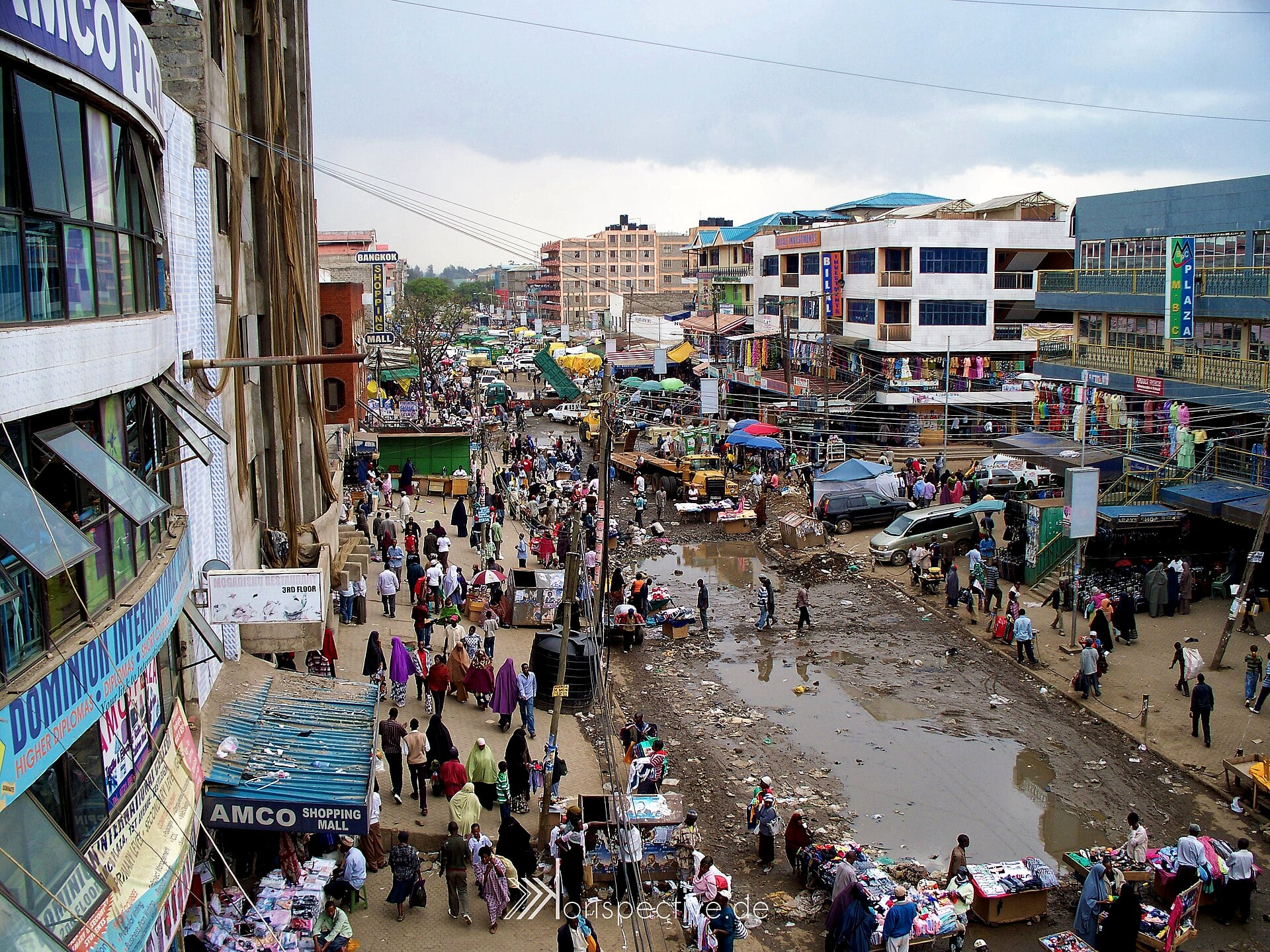 Crowded street market in Eastleigh, Nairobi, with shops, stalls and multi-storey buildings under a cloudy sky