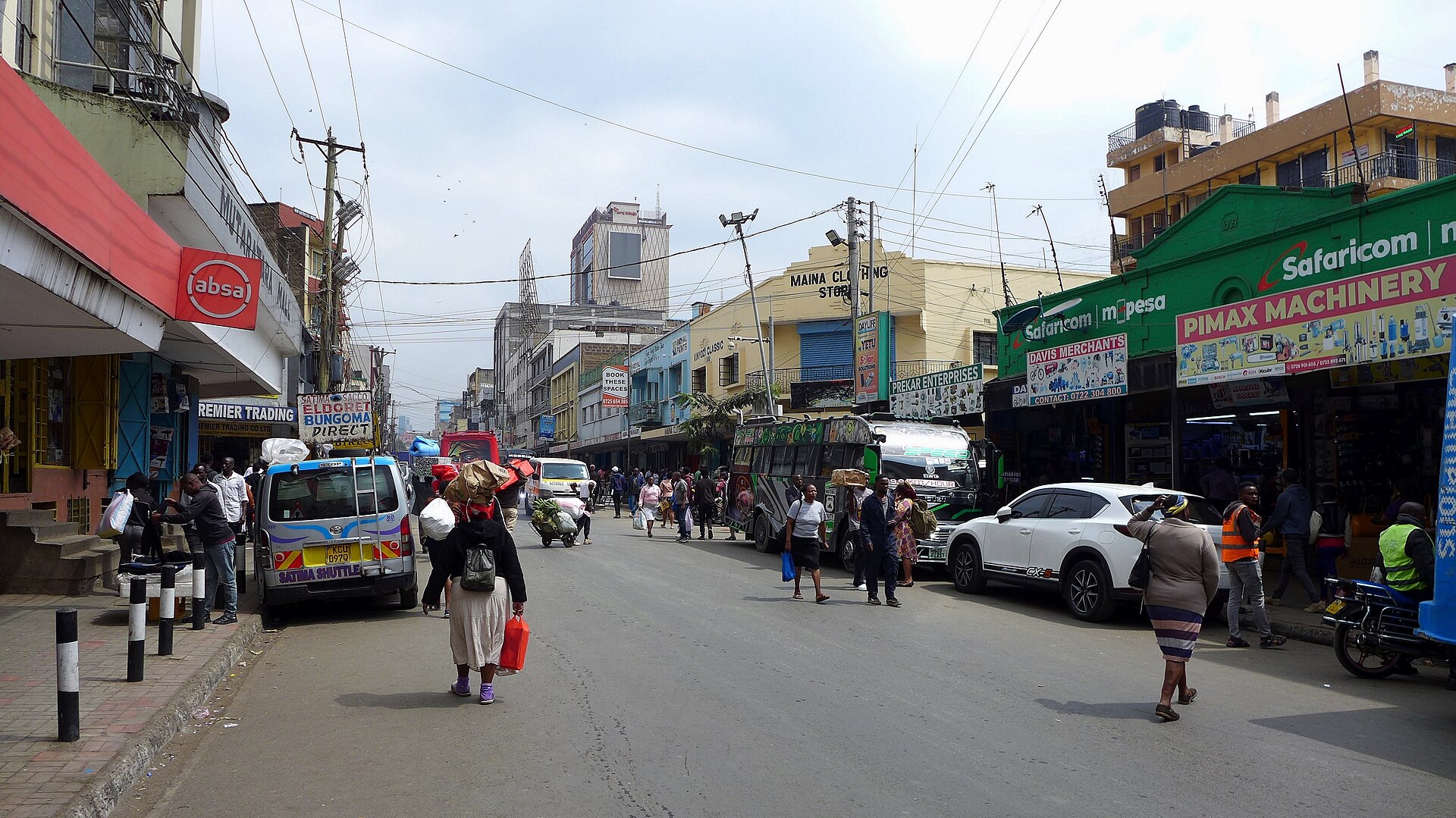 Pedestrians, minibuses and shopfronts on River Road, a busy street in central Nairobi, under a cloudy sky