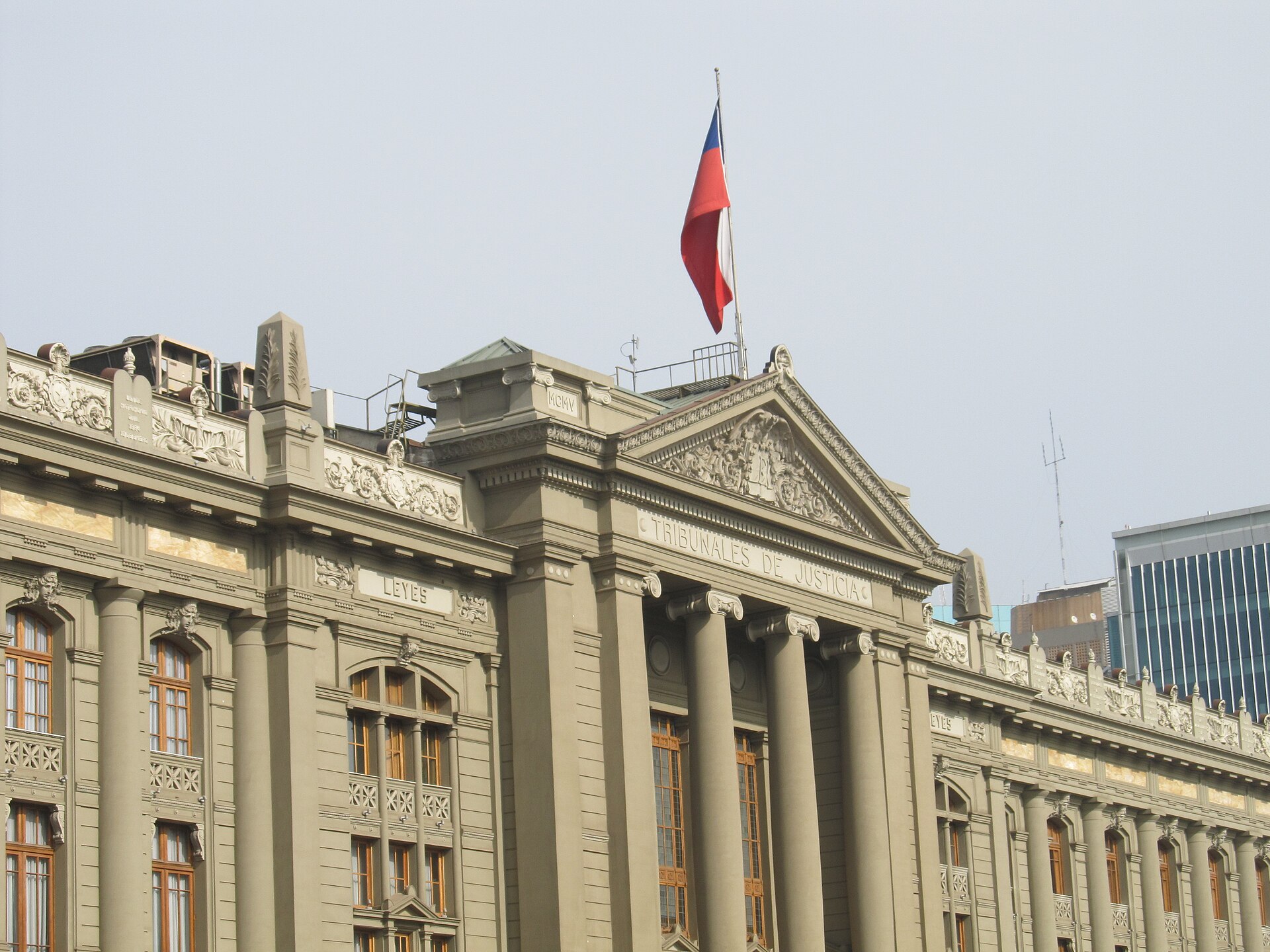 The pediment and columns of the Palace of Justice in Santiago under a grey sky, with the inscription Tribunales de Justicia and a Chilean flag