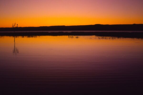 Lake Baringo in Kenya's Rift Valley under an orange sky, calm water and a low ridge on the horizon