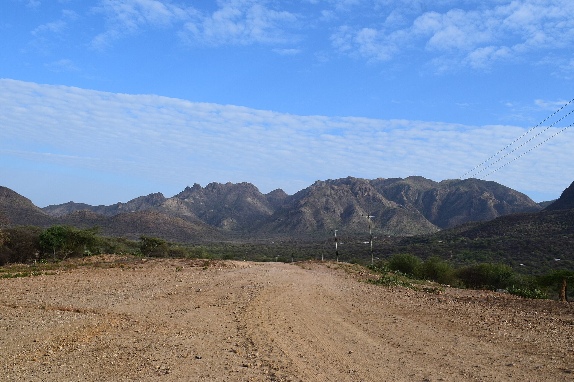 An unpaved dirt road leading towards rocky mountains under a blue sky in Tiaty, Baringo County, Kenya