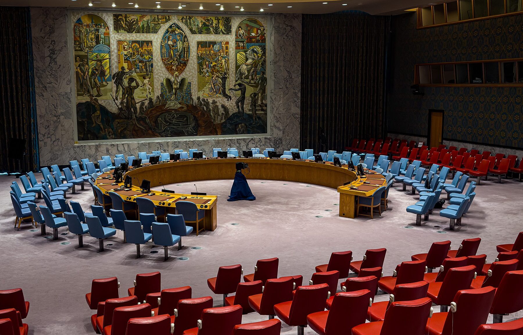The empty Security Council chamber at UN headquarters in New York, with the horseshoe table, blue and red chairs and a large mural