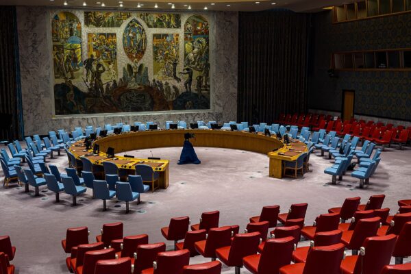 The empty UN Security Council chamber in New York, with the horseshoe table, blue and red delegate chairs and the large mural on the back wall