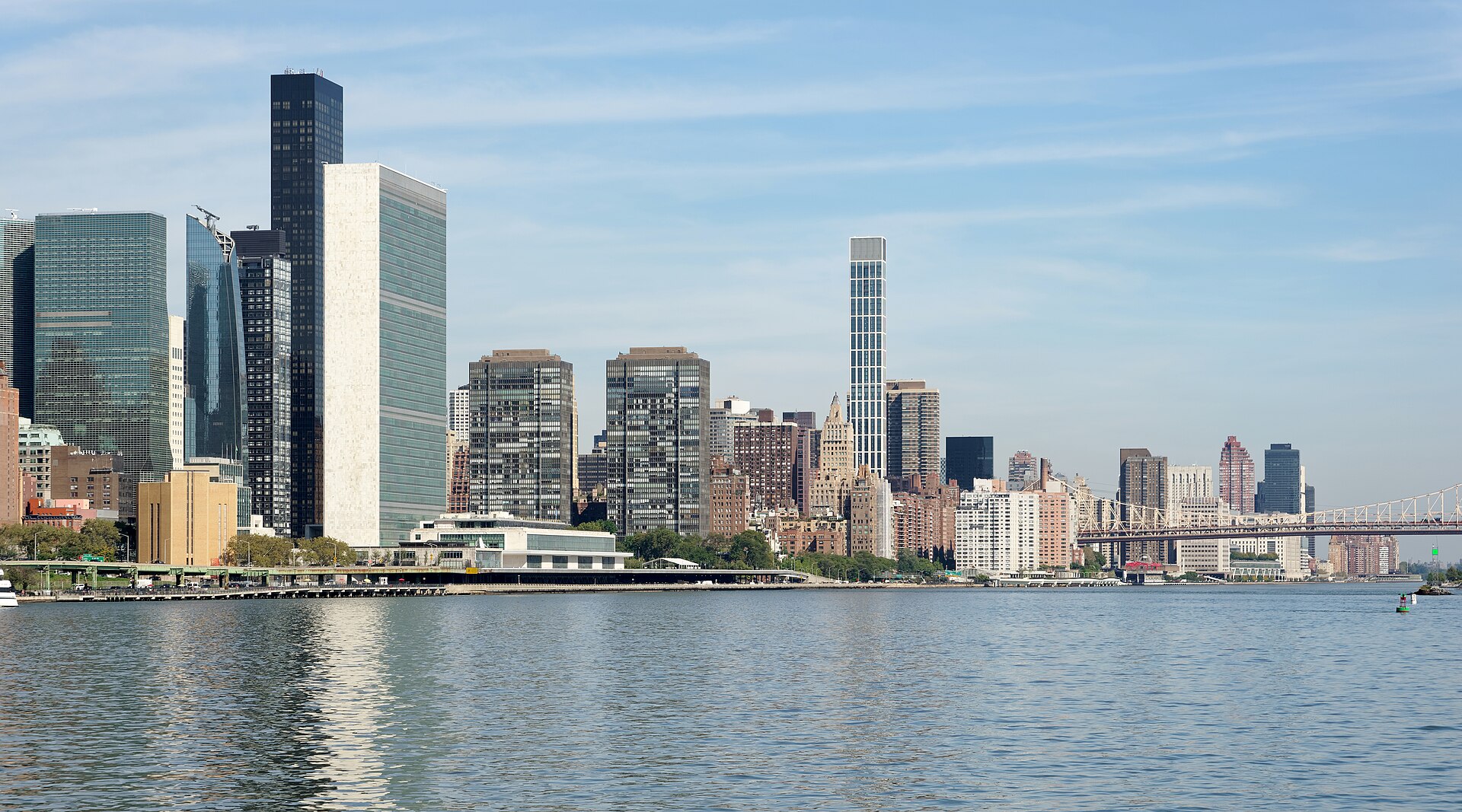 The glass towers of the UN headquarters complex and Manhattan buildings seen across the East River under a blue sky