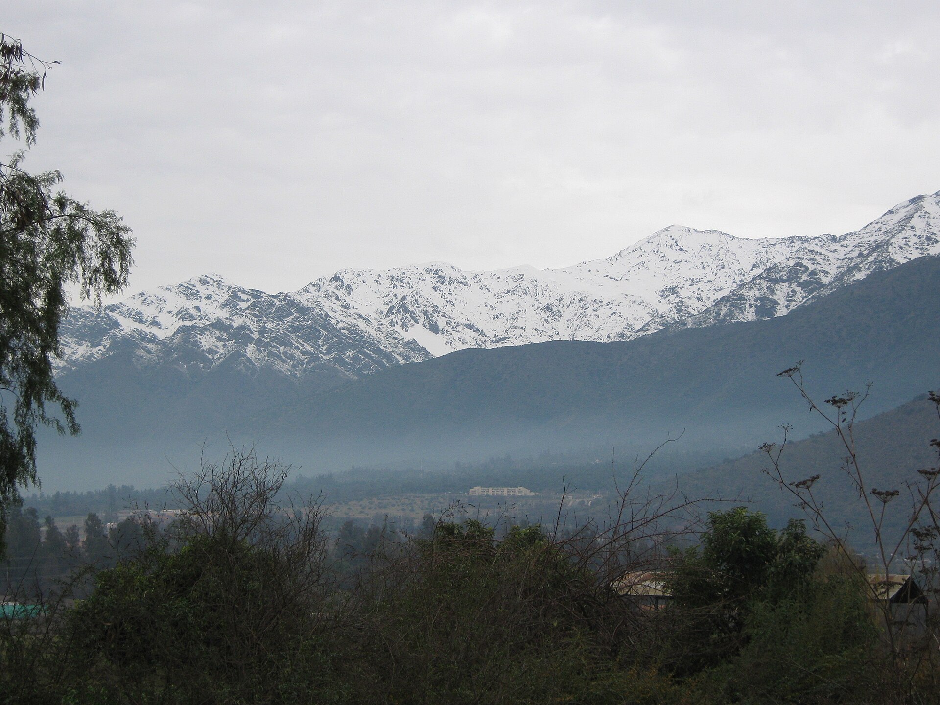Snow-capped Andes ridge above misty foothills and trees seen from Lo Cañas, Santiago