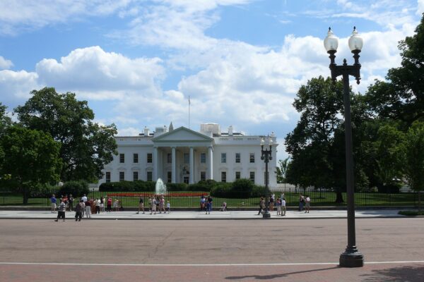 Visitors on the pavement in front of the White House fence on Pennsylvania Avenue under a cloudy sky