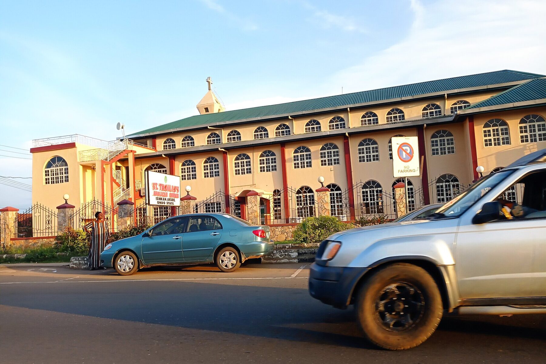 A pink and cream church building with a green roof beside a street in Akure, Ondo State, Nigeria, with cars in the foreground