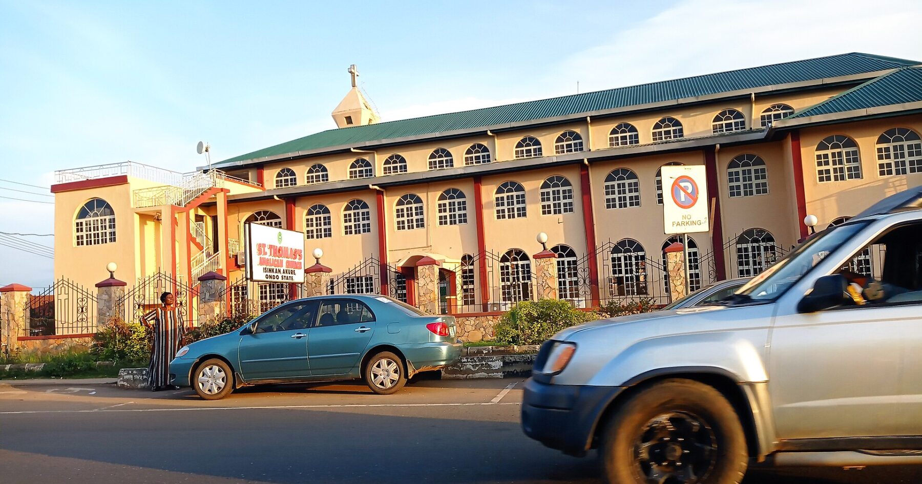 A pink and cream church building with a green roof beside a street in Akure, Ondo State, Nigeria, with cars in the foreground