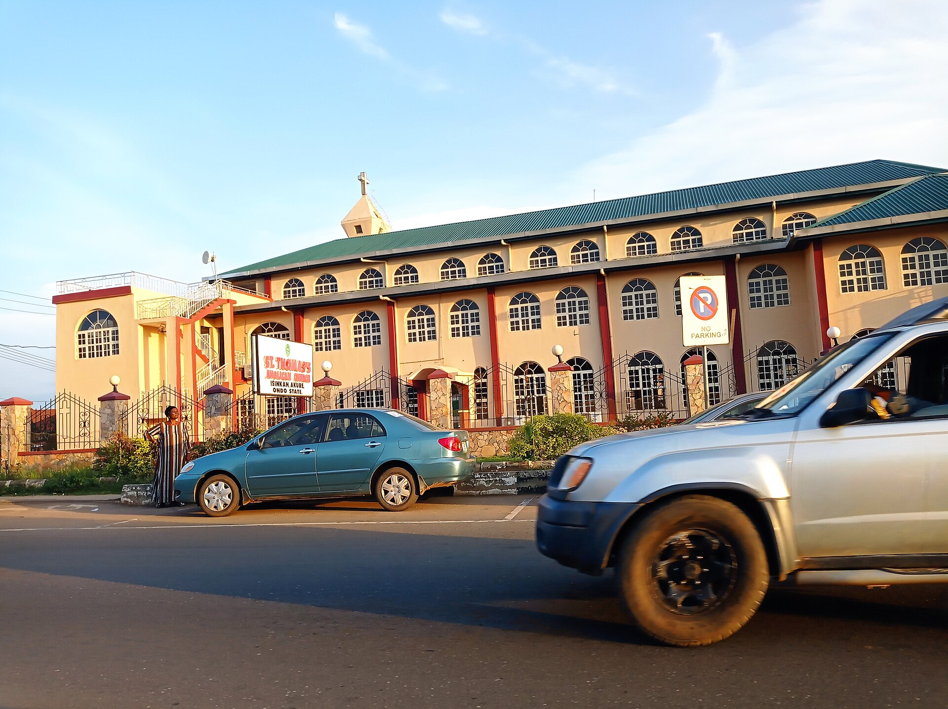 A pink and cream church building with a green roof beside a street in Akure, Ondo State, Nigeria, with cars in the foreground