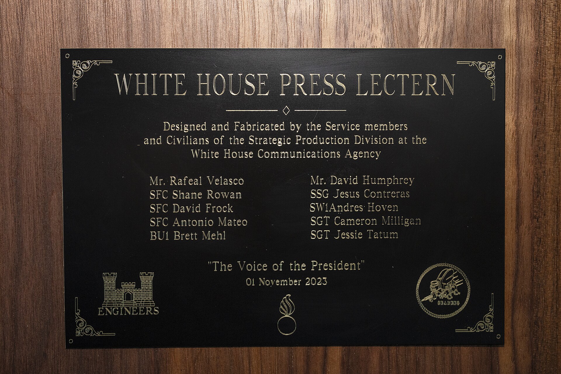 A black and gold plaque reading White House Press Lectern on a wooden panel, with the words The Voice of the President