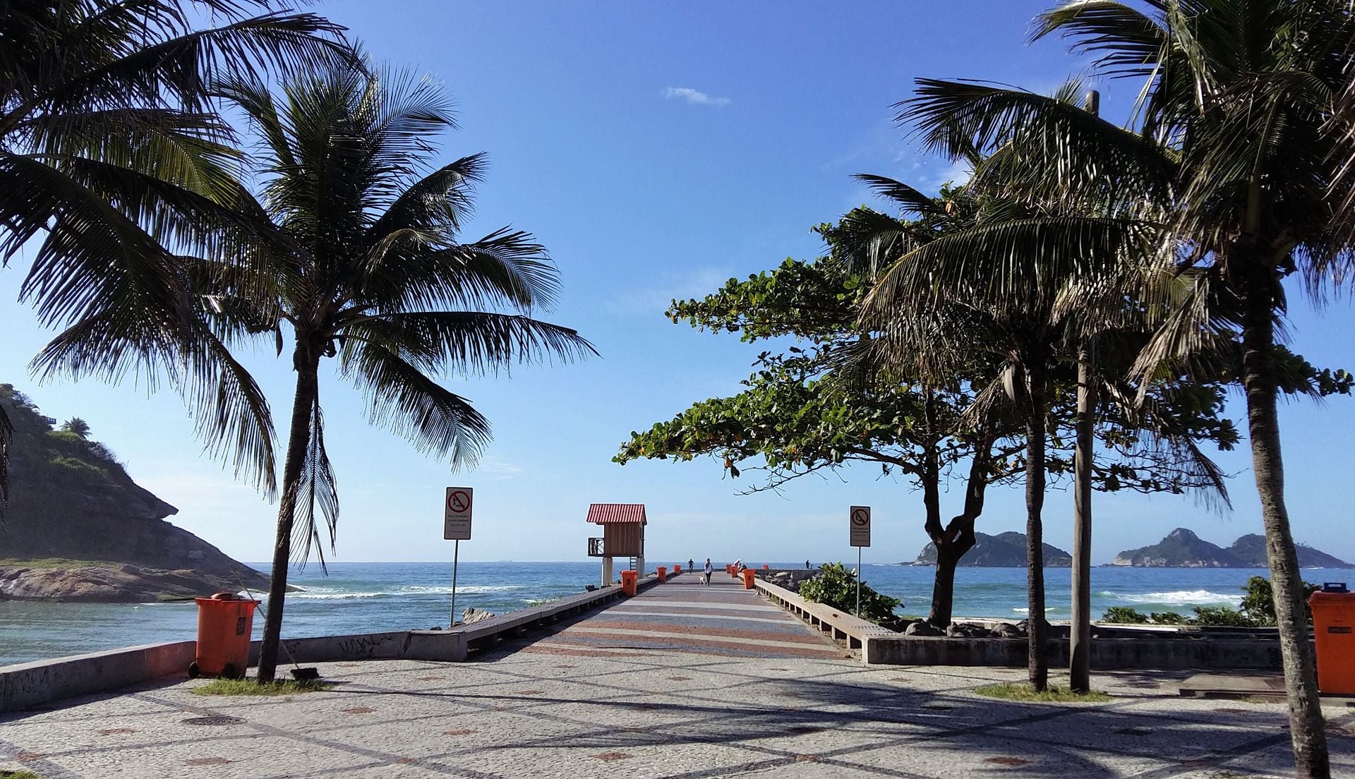 Walkway leading onto the Quebra-Mar breakwater in Barra da Tijuca, Rio de Janeiro, with palm trees and the open sea
