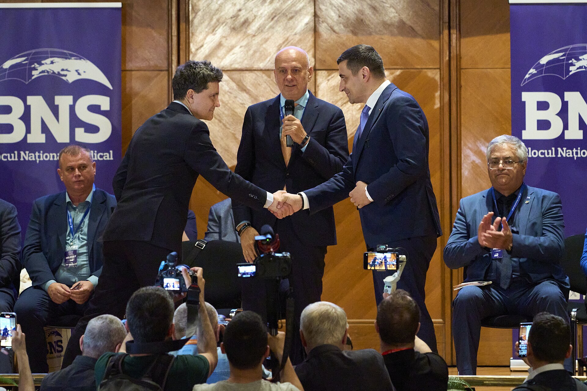 Nicusor Dan and George Simion shake hands on a stage during the 2025 runoff campaign