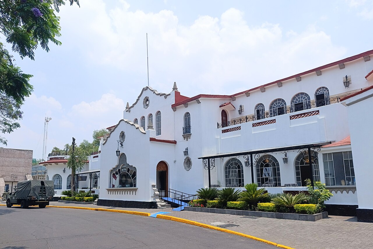 White Spanish-style clubhouse of the Casino Militar at Campo Marte in Mexico City, with palms and a flowerbed in front.