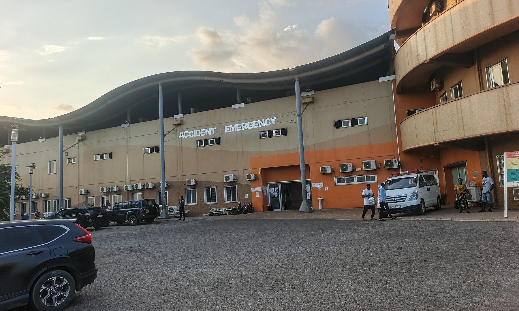 Accident and Emergency building of Komfo Anokye Teaching Hospital in Kumasi with parked cars and people outside at dusk
