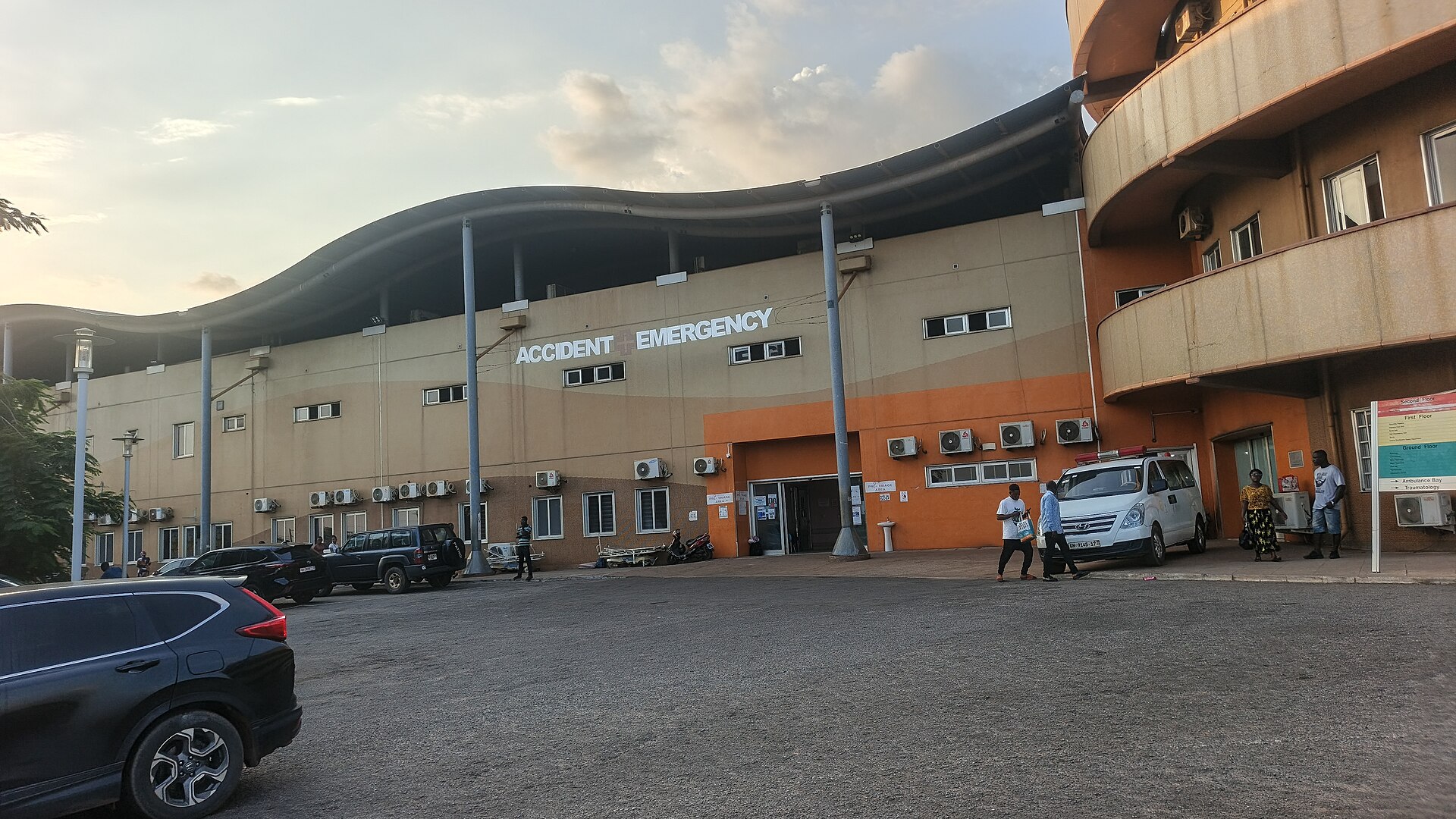 Accident and Emergency building of Komfo Anokye Teaching Hospital in Kumasi with parked cars and people outside at dusk