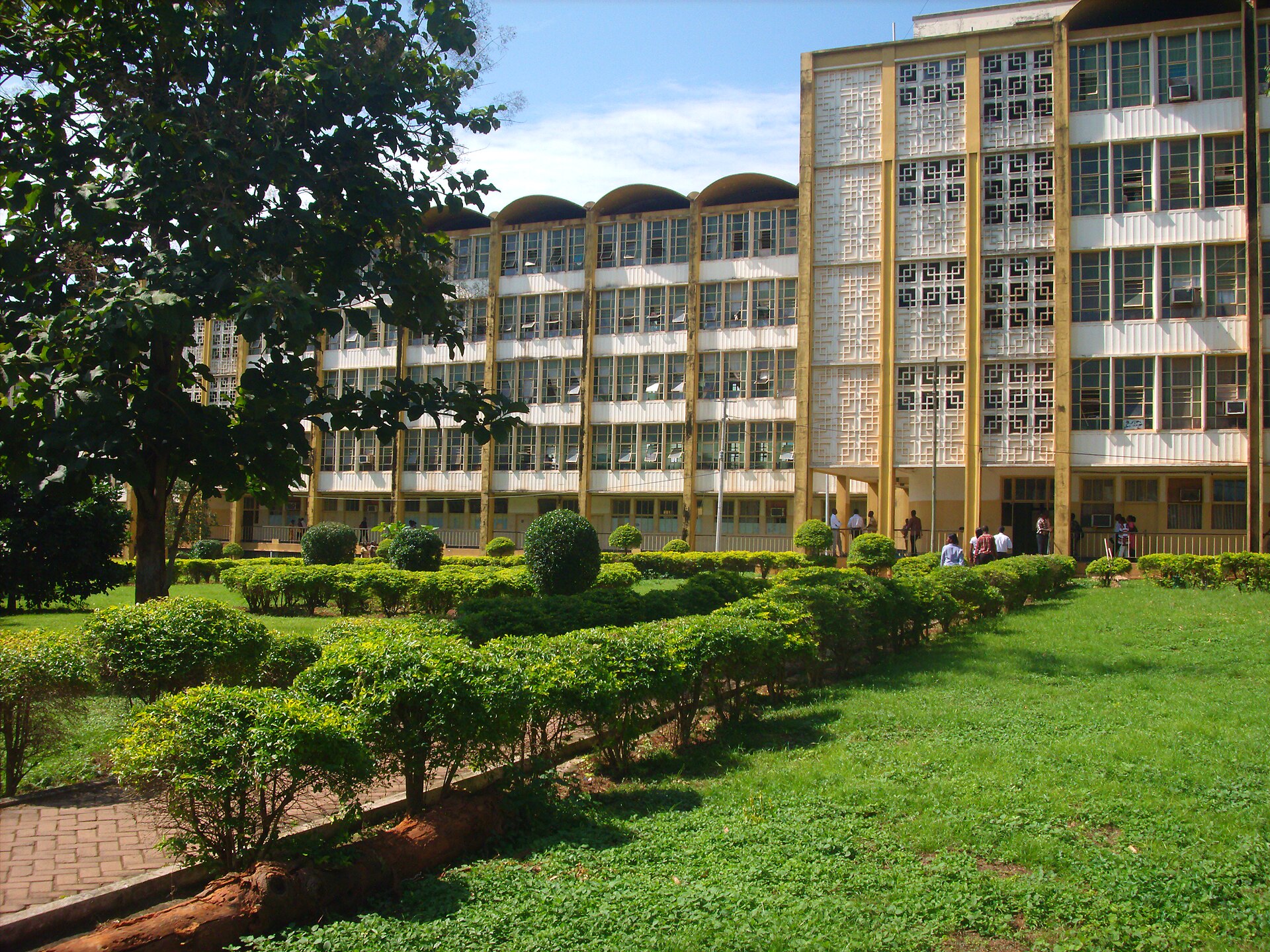 Multi-storey buildings of Komfo Anokye Teaching Hospital behind a lawn and trimmed hedges under a blue sky