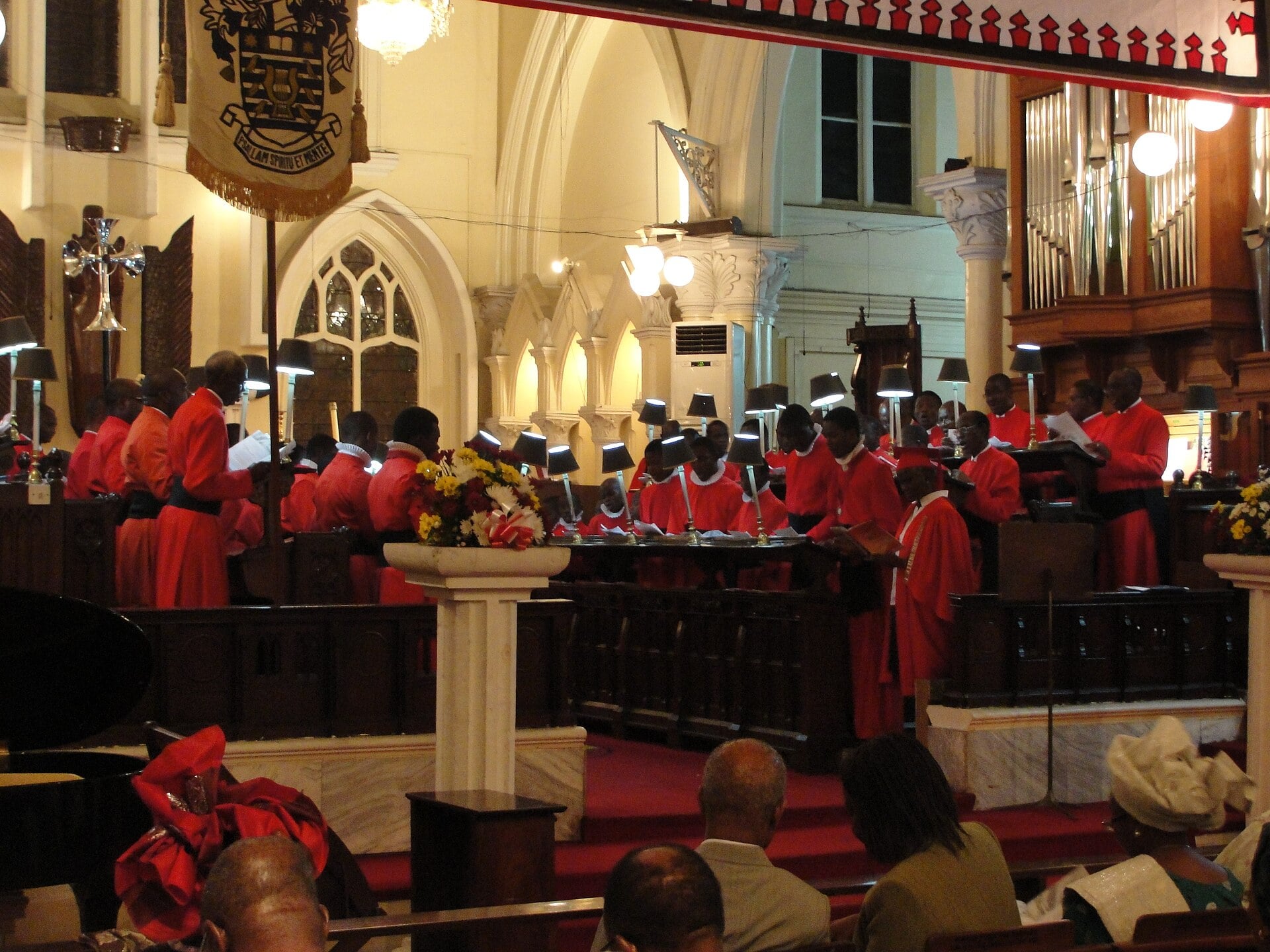 A robed church choir in red sings in the stalls of Christchurch Cathedral in Lagos, with the congregation seated in the foreground