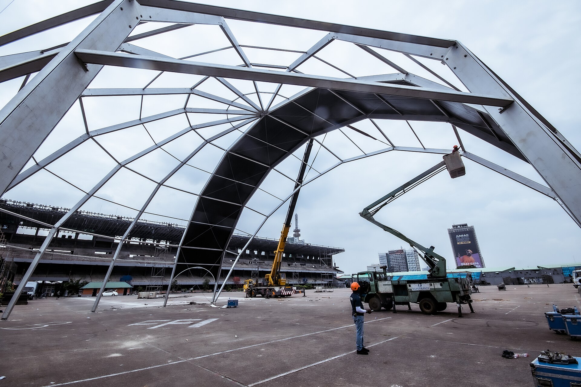 A worker in a hard hat watches cranes raise the steel frame of a large concert stage roof on Tafawa Balewa Square in Lagos