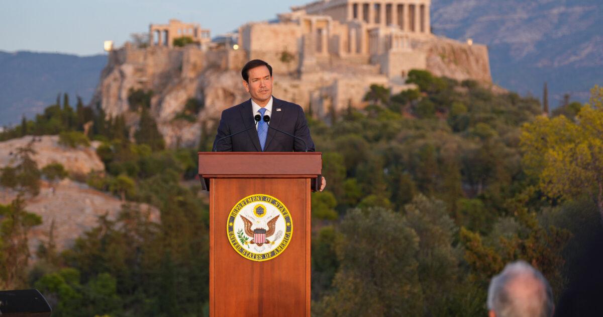 Marco Rubio speaking at a lectern on the Pnyx in Athens with the Acropolis behind him